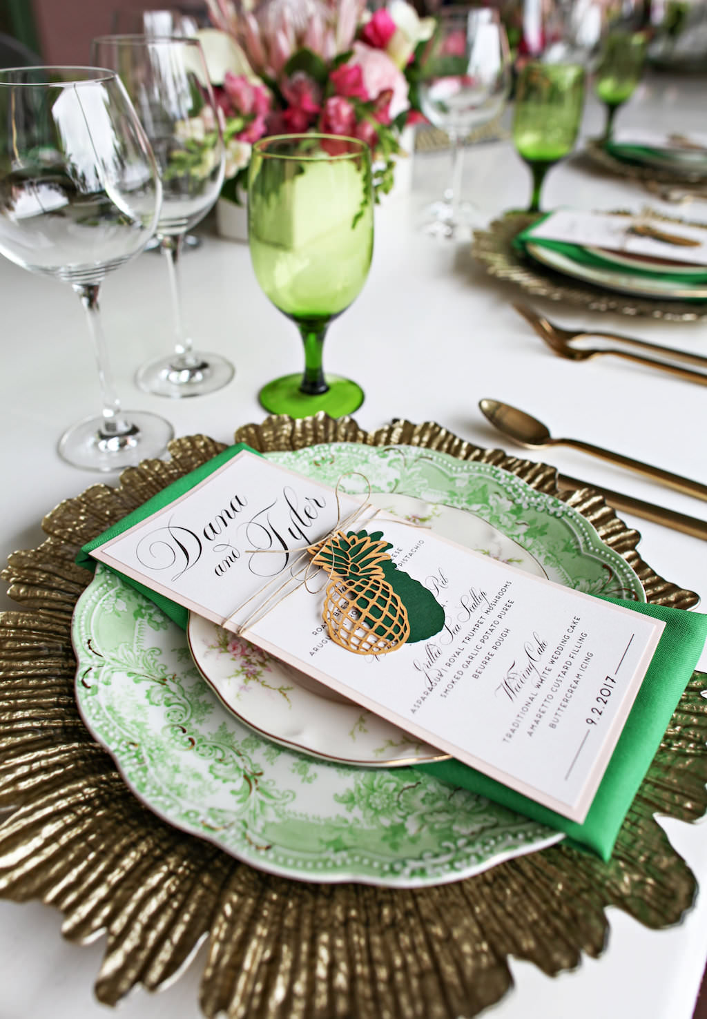 Old World Havana Tropical Inspired Wedding Reception Table Setting with Gold Charger, Vintage China Plates, Brushed Gold Flatware, Green Satin Linens and Laser-cut Pineapple Menu with Twine, and Colored Drinking Glasses | Tampa Bay Wedding Rentals A Chair Affair