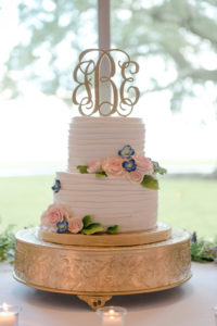 Two Tier Round White Wedding Cake on Gold Cakestand with Stylish Gold Monogram Cake Topper and Pink and Blue Icing Flowers with Greenery | Tampa Bay Wedding Cake Alessi Bakery