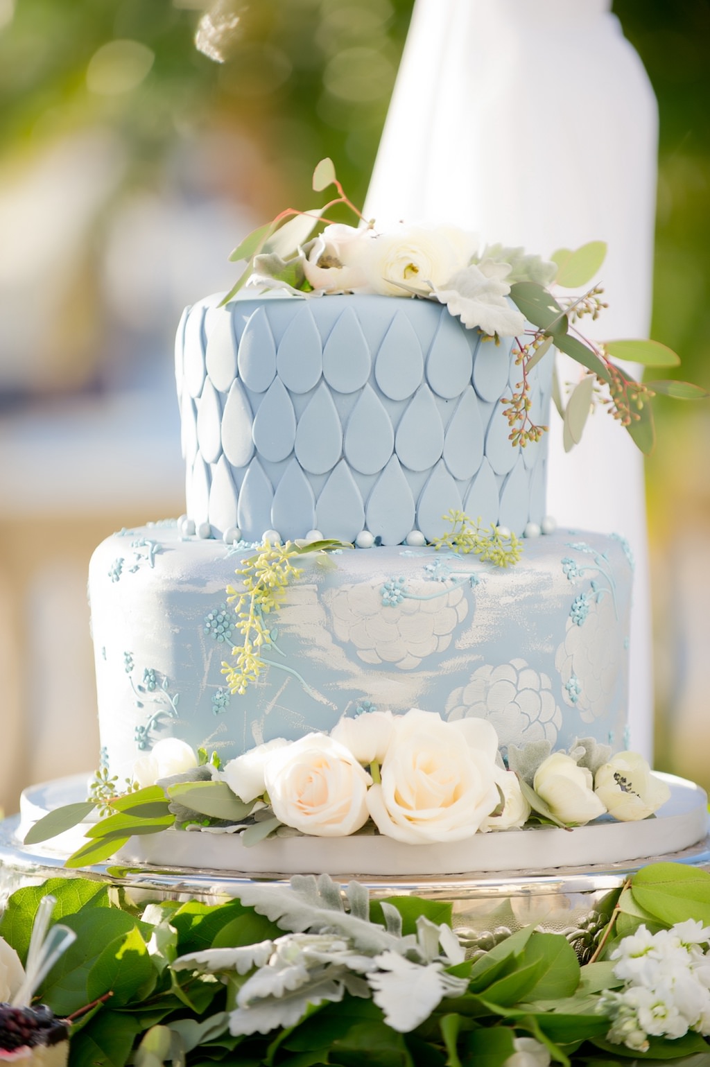 Two Tiered Hand-painted Light Blue and White Wedding Cake with White Floral Cake Topper with Greenery on Silver Cakestand for Outdoor French Countryside Inspired Wedding | Tampa Bay Wedding Cake and Dessert Bakery Alessi Bakery