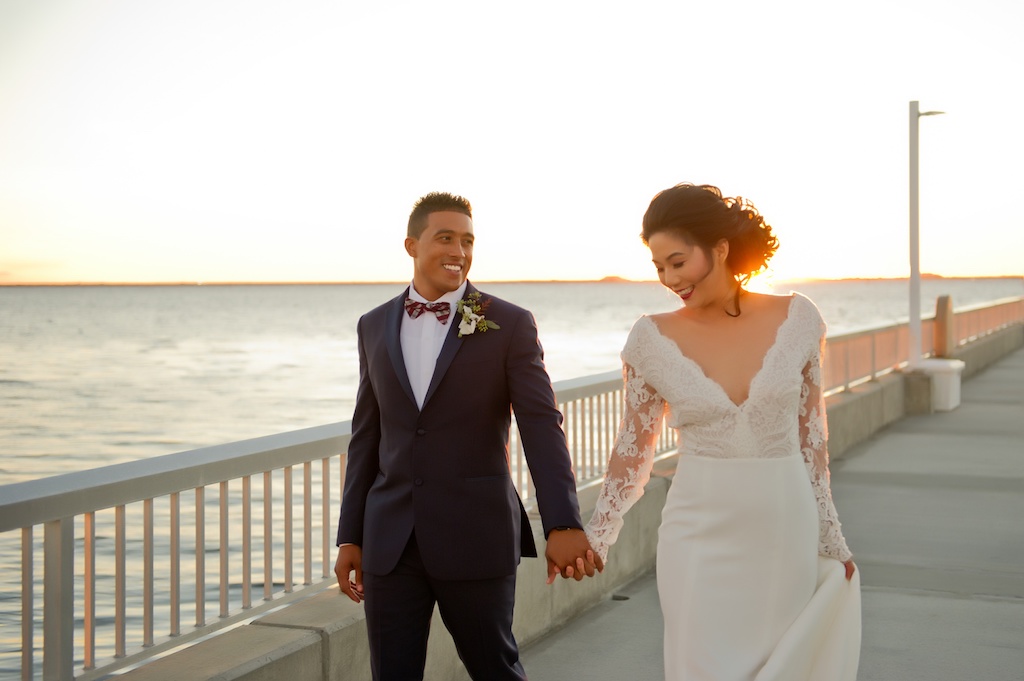 Waterfront Sunset Bride and Groom Wedding Portrait, Groom with Red and White Plaid Bowtie and Blue Suit, Bride in V Neck Lace Long Sleeve Daalarna Couture Wedding Dress | Tampa Wedding Photographer Andi Diamond Photography