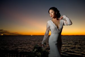 Waterfront Sunset Bridal Portrait, Bride in V Neck Lace Long Sleeve Daalarna Couture Wedding Dress | Tampa Wedding Photographer Andi Diamond Photography | Tampa Bridal Wedding Dress Shop The Bride Tampa | Tampa Bay Wedding Hair and Makeup Michele Renee The Studio