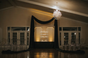 Modern, Sophisticated Black and White Wedding Ceremony Decor with Black Draping, Clear Plastic Chairs, and Pillar Candles in Glass Hurricane Lanterns | Dade City Florida Ballroom Wedding Venue Stonebridge at the Lange Farm | Tampa Bay Wedding Planner UNIQUE Events | Wedding Rentals A Chair Affair