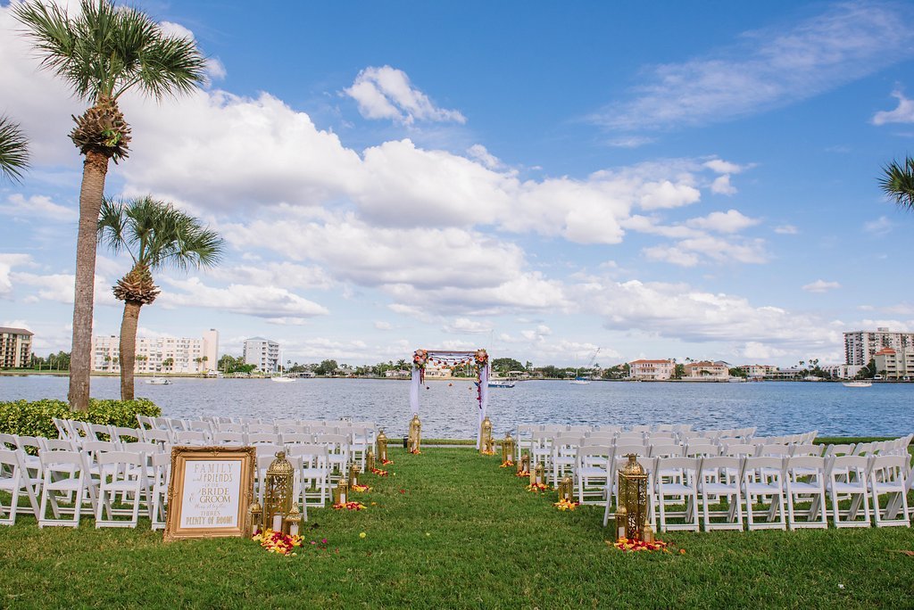 Outdoor Waterfront Jewel Tone Whimsical Wedding Ceremony with Gold Lanterns and Yellow and Red Rose Petals with Folding White Chairs and White Drapery and Floral Ceremony Arch | Tampa Bay Outdoor Wedding Ceremony Venue Clearwater Beach Recreation Center | Planner Special Moments Event Planning