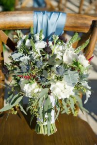 Wild Greenery and White Floral with Thistle Wedding Bouquet on Wooden Cross Back Chair with Blue Ribbon