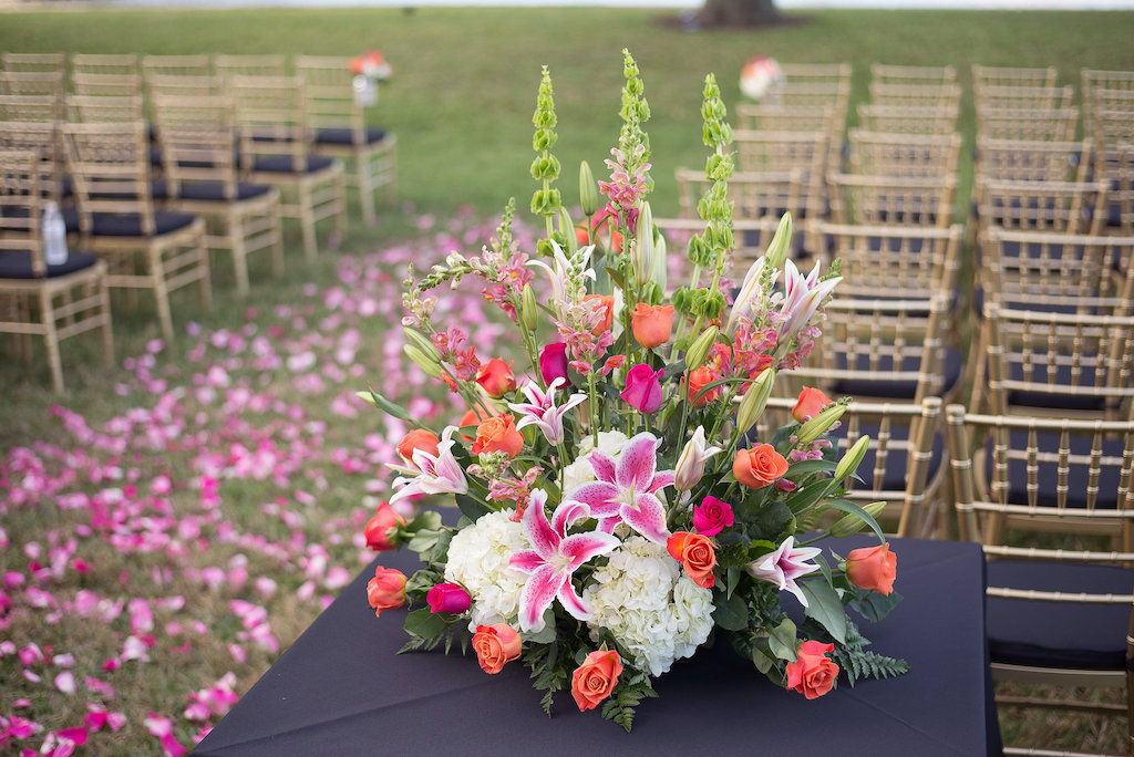 Outdoor Tropical Old Florida Themed Wedding Ceremony with Gold Chiavari Chairs with Black Cushions and Orange Rose, White Hydrangea, Pink Lily and Greenery Centerpiece and Pink Tropical Petal Aisle