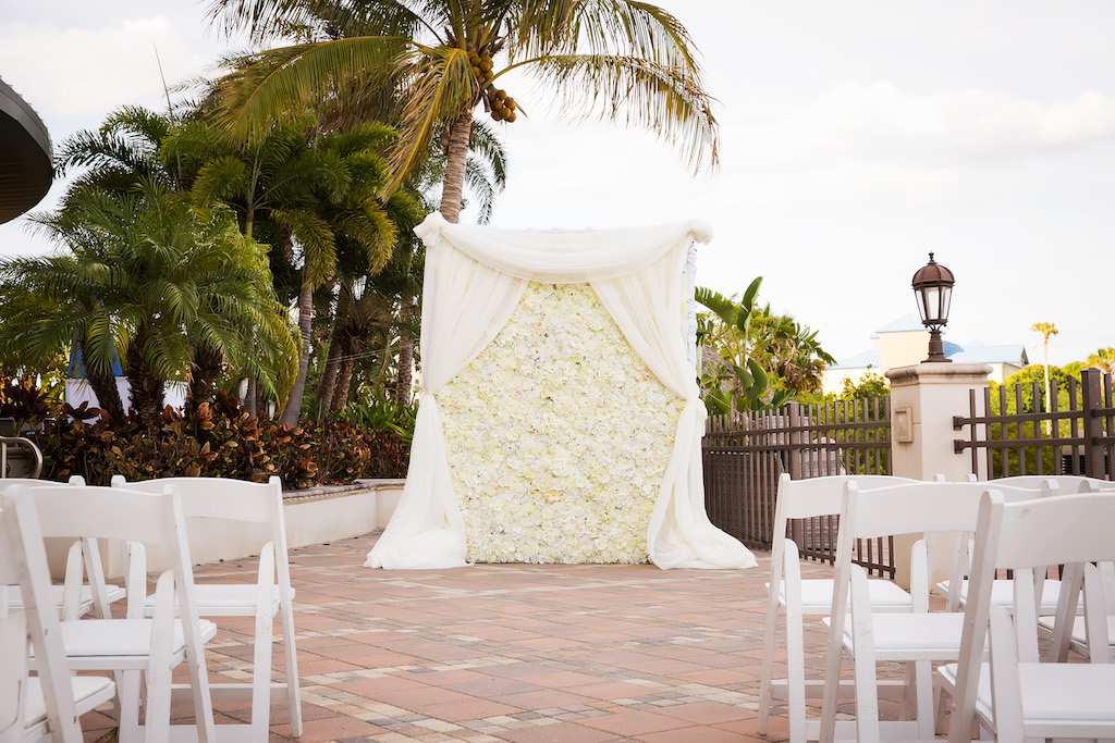 Hotel Courtyard Garden Ceremony with White Floral and Drapery Ceremony Backdrop and White Folding Chairs | Waterfront Hotel Wedding Venue The Westin Tampa Bay