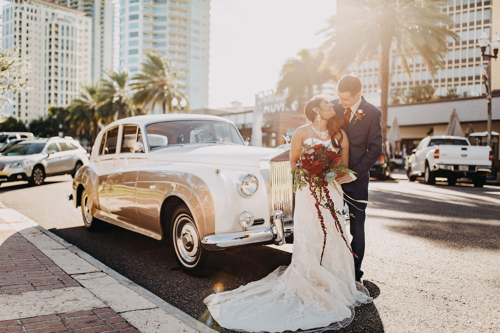 Downtown St Pete Blue and Red Modern Indian Wedding Bride and Groom Portrait with antique Car, Bride in Lace Strapless Davids Bridal Dress, Groom in Navy Suit with Red Tie and Boutonniere, Red and Plum Floral with Greenery Bouquet | St Pete Wedding Photographer Rad Red Creative | Menswear Sacino's Formalwear