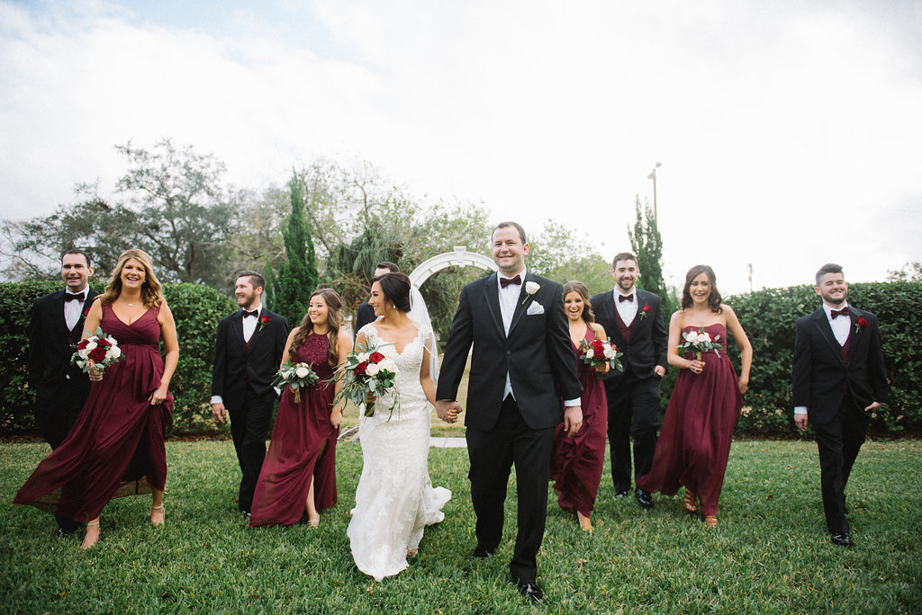 Outdoor Garden Wedding Party Portrait, Bride with White, Red Rose and Greenery Bouquet, Bridesmaids in Mismatched Burgundy Red David's Bridal Dresses, Groomsmen in Black Tuxedos with Dark Red Vests and Red Rose Boutonniere | Tampa Bay Wedding Photographer Kera Photography | Garden Wedding Venue Davis Island Garden Club