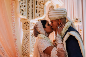 Regal and Romantic Traditional Hindu Indian Wedding Ceremony Bride and Groom First Kiss Portrait with Gold Uplighting and Blush Pink Draping Behind the Mandap | Tampa Bay Wedding Venue Safety Harbor Resort and Spa | Planner Glitz Events | Photographer Grind and Press Photography