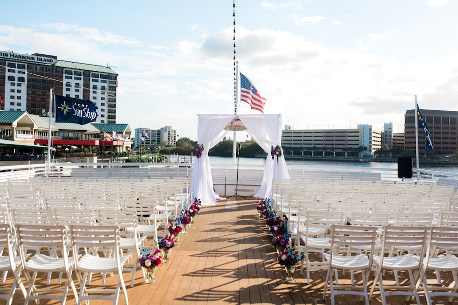 Outdoor Wedding On the Water Wedding Ceremony with White Folding Chairs, White Draped Chuppah Wedding Arch with Purple, Blue, White, and Red Flower Arrangements | Tampa Bay Nautical Wedding Venue Yacht StarShip