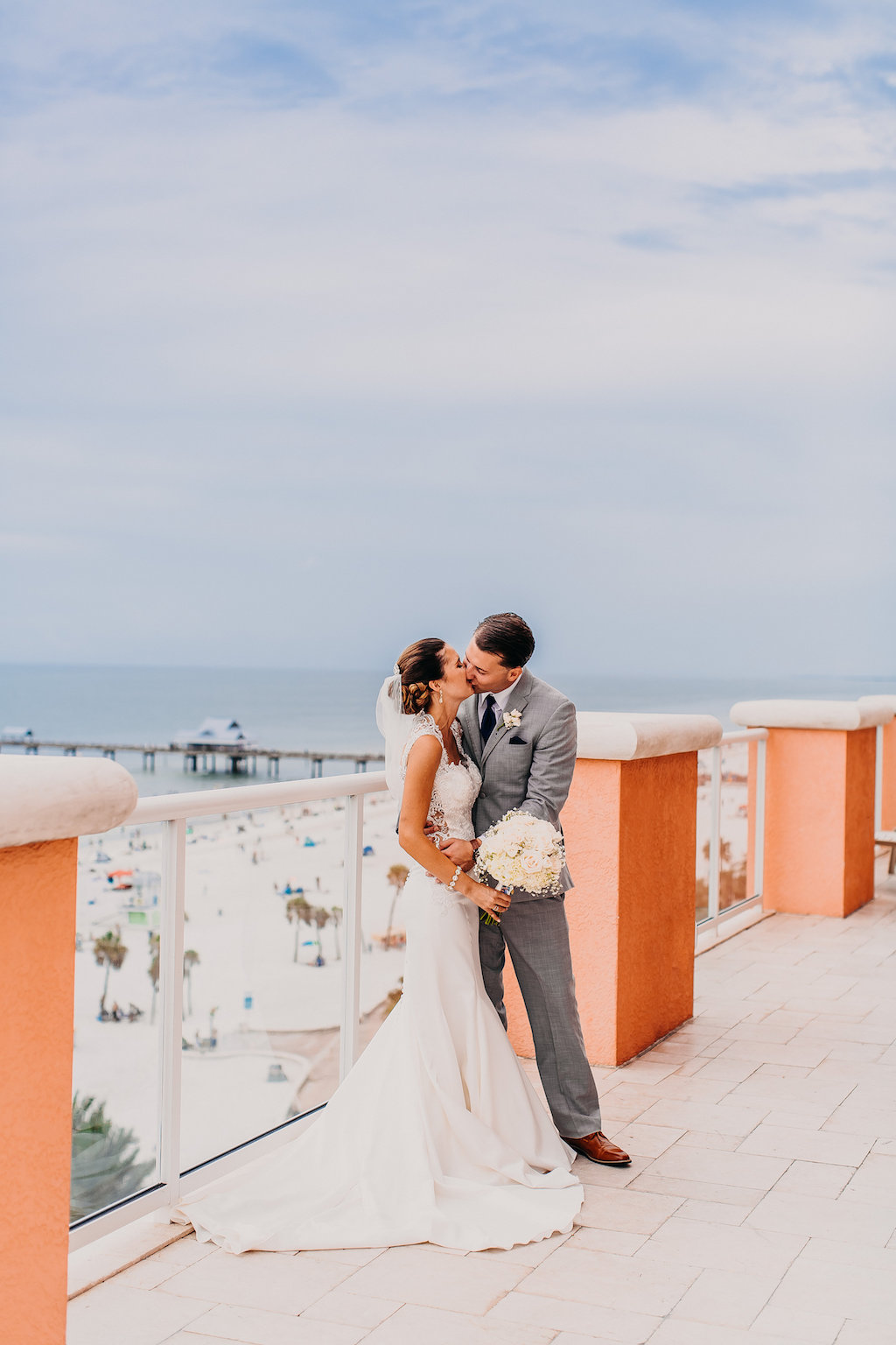 Outdoor Rooftop Bride and Groom Wedding Portrait, Bride in Lace Illusion Back Sincerity Bridal Wedding Dress, Groom in Gray Suit with Navy Blue Tie and White Floral Boutonniere | Tampa Bay Beachfront Hotel Wedding Venue Hyatt Regency Clearwater Beach | Wedding Photographer Rad Red Creative