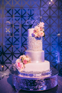 Four Tier Round White and Silver Wedding Cake with Pink Roses and Greenery, on Silver Cake Stand with Stylish Custom Monogrammed Cake Topper