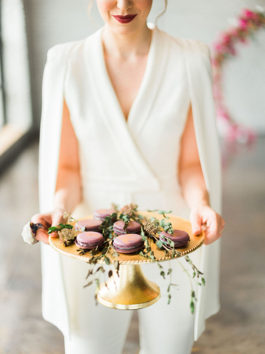 Bride in Lavish Alice White Jumpsuit with Cape with Modern Wedding Gold and Purple Macaroons on Gold Cake Stand with dried greenery