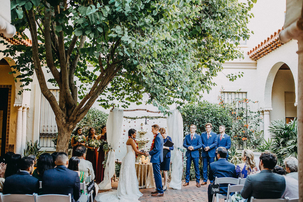 Outdoor Garden Modern Indian Wedding Ceremony Portrait Decor with Hanging Blush, Red, and Orange Rose Garland and White Draped Arch, Groom and Groomsmen in Blue Suits, Bridesmaids in Red Dresses | Tampa Bay Wedding Venue St Petersburg Museum of Fine Arts | Wedding Photography Rad Red Creative | Menswear Sacino's Formalwear