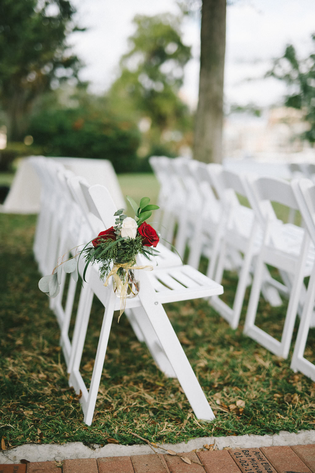 Outdoor Garden Wedding Ceremony Decor with White Wooden Folding Chairs, and Red and White Rose with Greenery Flowers with Twine