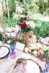 Outdoor Whimsical Boho Garden Wedding Reception Decor with Vintage Mismatched Dishes and Garland Floral Table Runner and Red and White Centerpiece