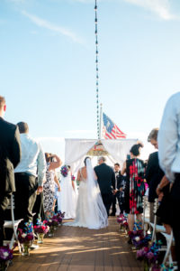 Outdoor On the Water Wedding Ceremony Portrait with White Folding Chairs, White Draped Chuppah Wedding Arch with Purple, Blue, White, and Red Flower Arrangements | Tampa Bay Nautical Wedding Venue Yacht StarShip
