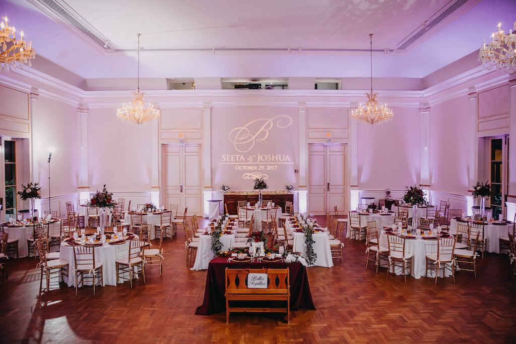 Modern Ballroom Wedding Reception with Tall Red and Greenery Centerpieces and Feasting Table Garlands, Purple Uplighting and Custom Bride and Groom Name Projection | Tampa Bay Wedding Venue St Petersburg Museum of Fine Art