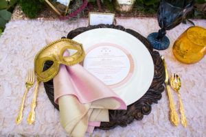 Outdoor Whimsical Boho Garden Wedding Reception Decor with Gold Venetian Mask, Wood Charger, Gold Flatware and Pink Textured Linen | Over the Top Rental Linens