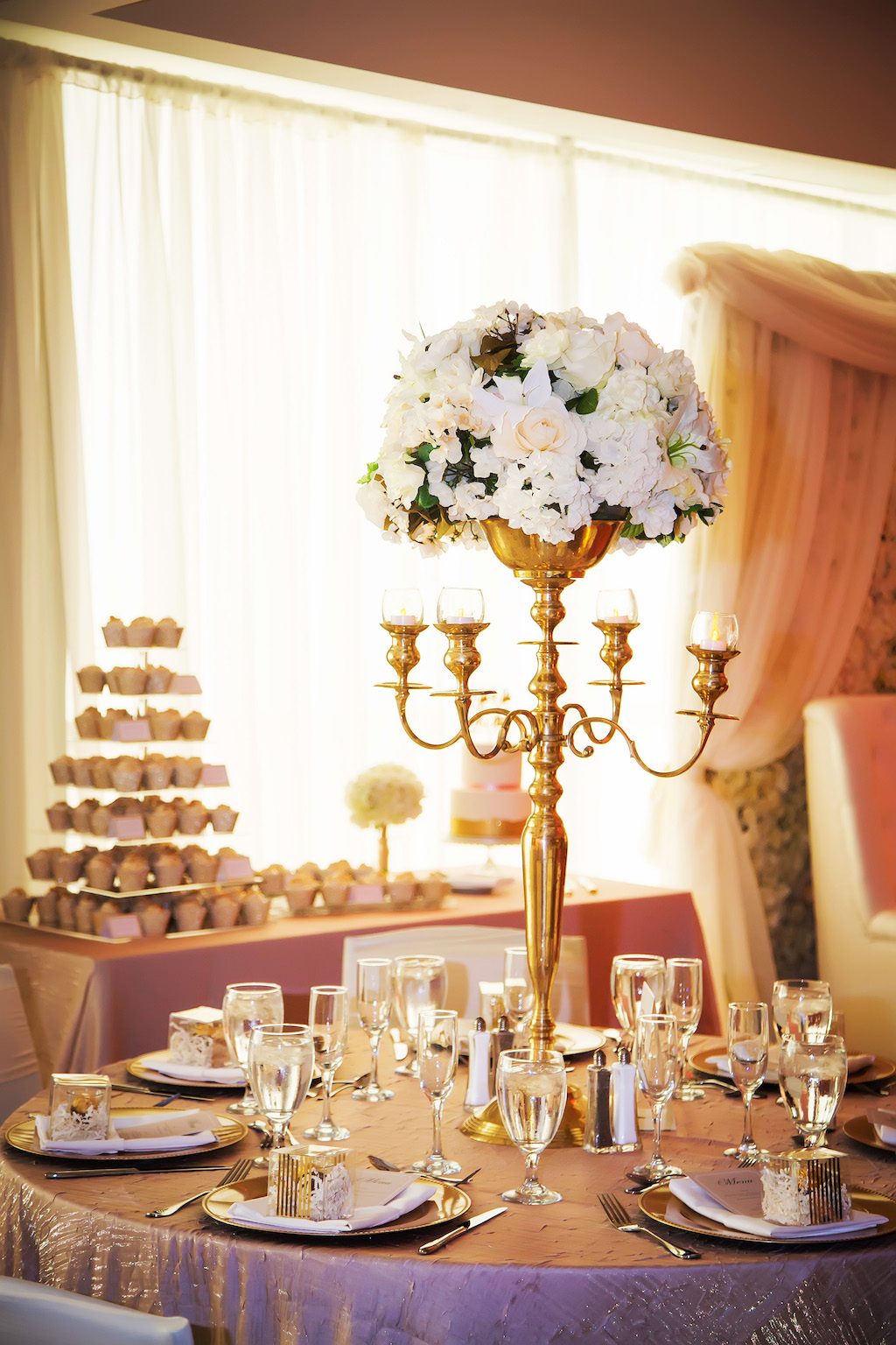 Luxurious Gold and White Wedding Reception with Round Tables with Blush and Gold Textured Table Cloths, Tall Gold Candelabra with White Floral Centerpieces, and Seven Tiered Cupcake Stand on Dessert Table | Hotel Wedding Reception Venue The Westin Tampa Bay