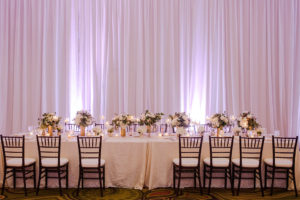 Hotel Ballroom Gold and White Wedding Reception Long Feasting Table with Black Chiavari Chairs, Low white and Greenery centerpieces in Gold Vases with votive candles and white draping | Tampa Bay Historic Wedding Venue The Vinoy