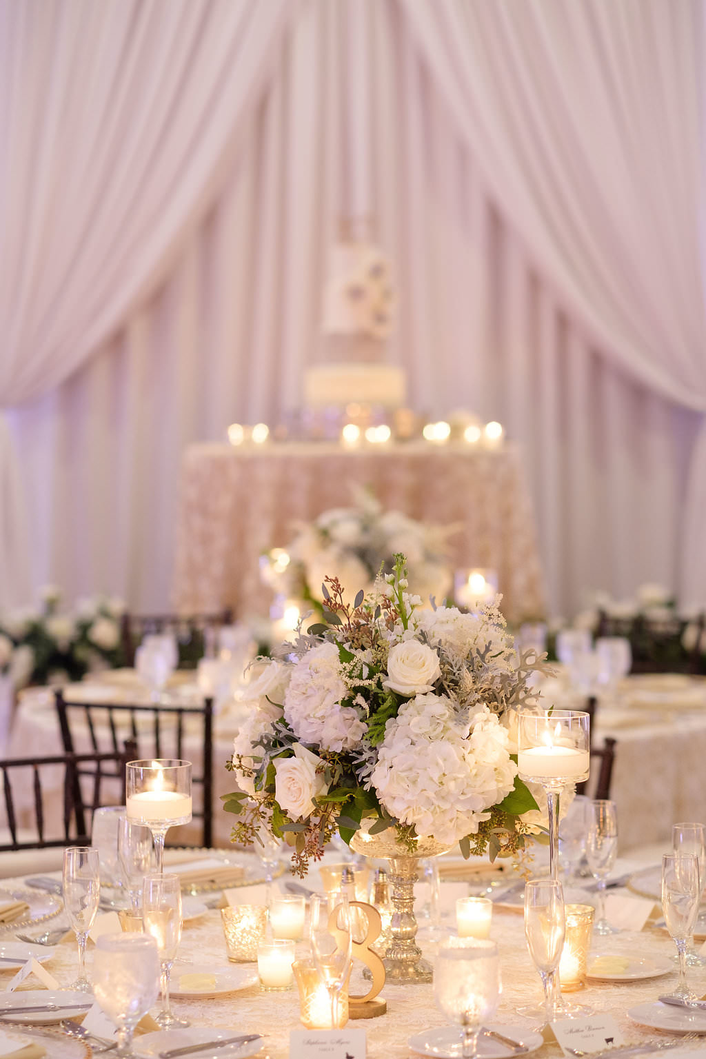 Hotel Ballroom Gold and White Wedding Reception Round Table Decor with Short White Hydrangea and greenery Centerpiece with votive candles and blush linens, and white draping | St Pete Historic Wedding Venue The Vinoy