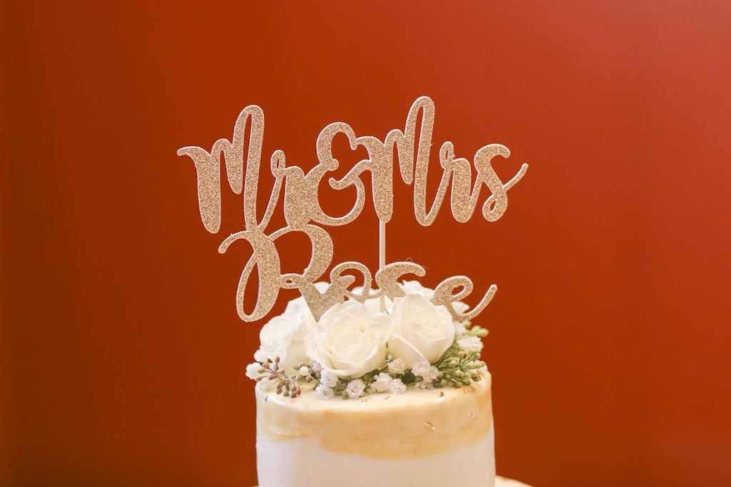 Mr and Mrs Custom Stylish Gold Glitter Cake Topper on Round Gold and White Cake with White Rose and Greenery