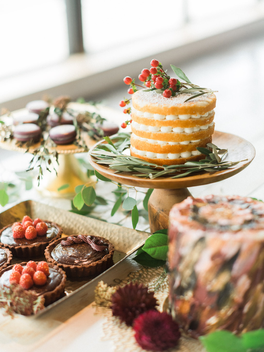 Modern Wedding Dessert Bar with Five Layer Round Bare Layer Cake, Chocolate Tarts, and Macaroons