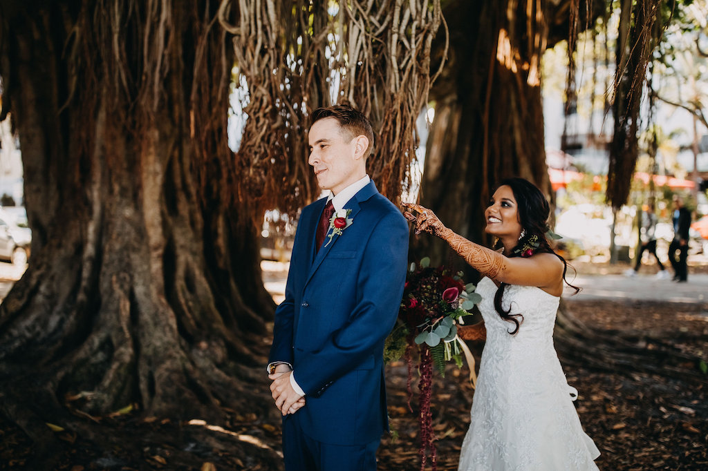 Blue and Red Modern Indian Wedding Outdoor First Look Portrait Under Banyan Tree, Bride in Lace Strapless Davids Bridal Dress, Groom in Navy Suit with Red Tie and Boutonniere, Red and Plum Floral with Greenery Bouquet | St Pete Wedding Photographer Rad Red Creative | Menswear Sacino's Formalwear