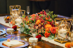 Intimate Wedding Reception Table Decor with Floating Votive Candles in Brass Geometric Holders with Red and Orange Floral Centerpiece with Greenery on Simple Linen Runner with Marble Place Cards and Gold Flatware | Tampa Wedding Planner UNIQUE Weddings and Events | Rentals Over The Top Linens