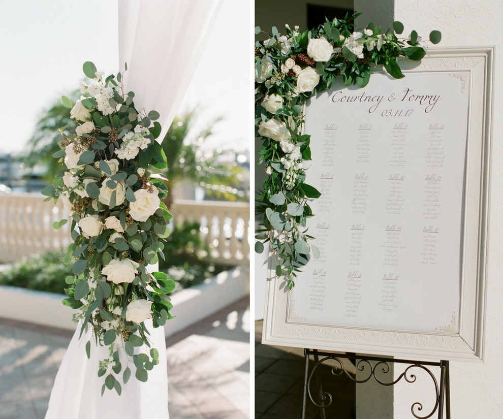Outdoor Waterfront Wedding Ceremony with White Draped Arch with White Roses and Natural Greenery, White Printed Seating Chart in Elegant Silver Frame | Tampa Bay Wedding Planner Unique Weddings and Events | Venue The Westshore Yacht Club