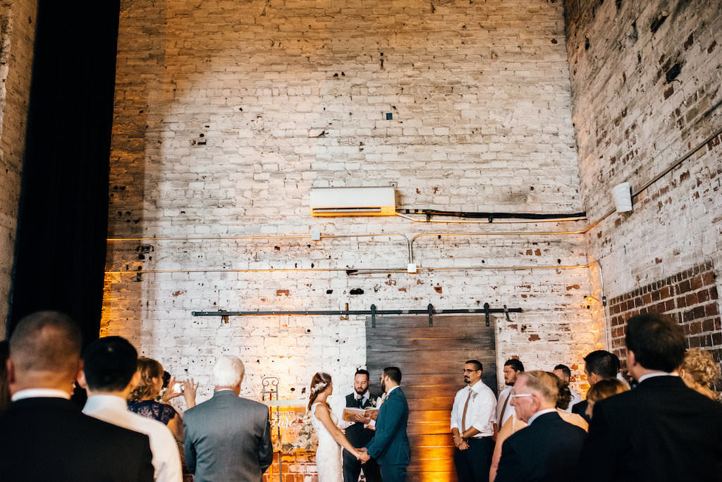 Vintage Travel Inspired Wedding Ceremony Portrait in front of Wood Barn Door with Brick Walls | Downtown Tampa Historic Wedding Venue The Rialto Theatre | Planner Glitz Events