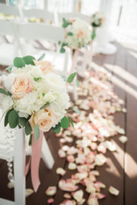 Outdoor Whimsical Beach Deck Wedding Ceremony Decor with White Folding Chairs with Blush Rose and White Hydrangea with Greenery and Long Pink Ribbon and Jewels, Pink Rose Petal Aisle