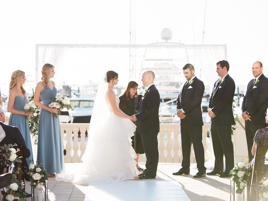 Outdoor Waterfront Wedding Ceremony Portrait, Bride in Layered Ballgown Dress, Bridesmaids in Long Dusty Blue Dresses, with White Rose and Greenery Bouquet, Groom and Groomsmen in Black Suits | Tampa Bay Wedding Venue The Westshore Yacht Club | Planner Unique Weddings and Events