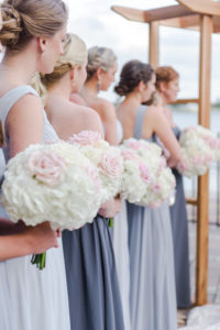 Outdoor Wedding Ceremony Bridesmaids Portrait in Mismatched Gray Dresses with White and Blush Pink Rose Bouquets and Wooden Ceremony Arch