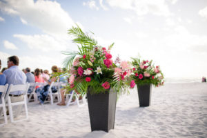 Outdoor Beach Wedding Ceremony Decor with Tall BLush, Pink, Magenta Rose, White Lilly, and Palm Frond Tropical Greenery Flower Arrangement in Wicker Planter, with White Folding Chairs | Tampa Bay Destination Wedding Planner NK Productions