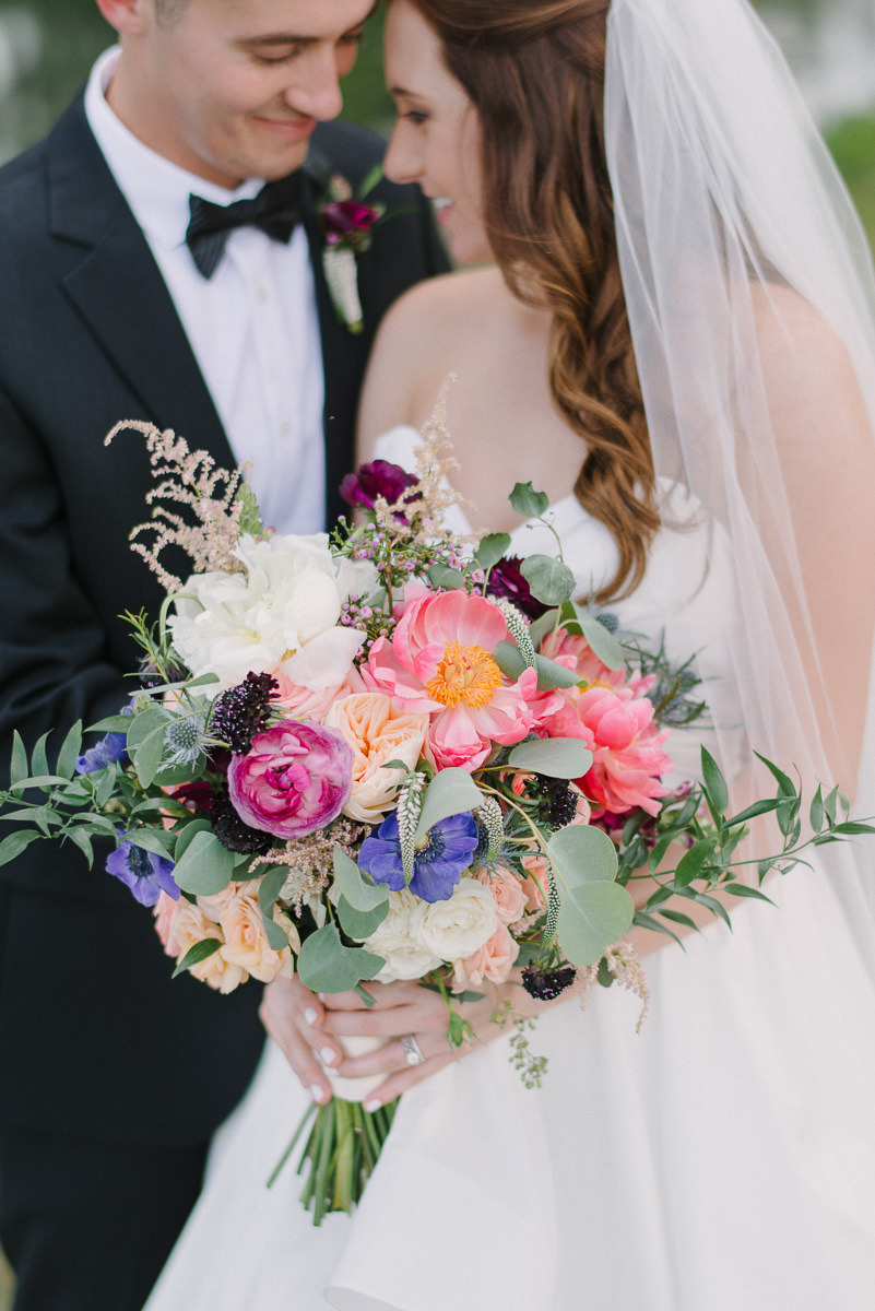 Outdoor Bride and Groom Portrait, with Pink, Peach, Purple, White Floral and Greenery Bouquet, Groom in Black Tux with Red Flower Boutonniere