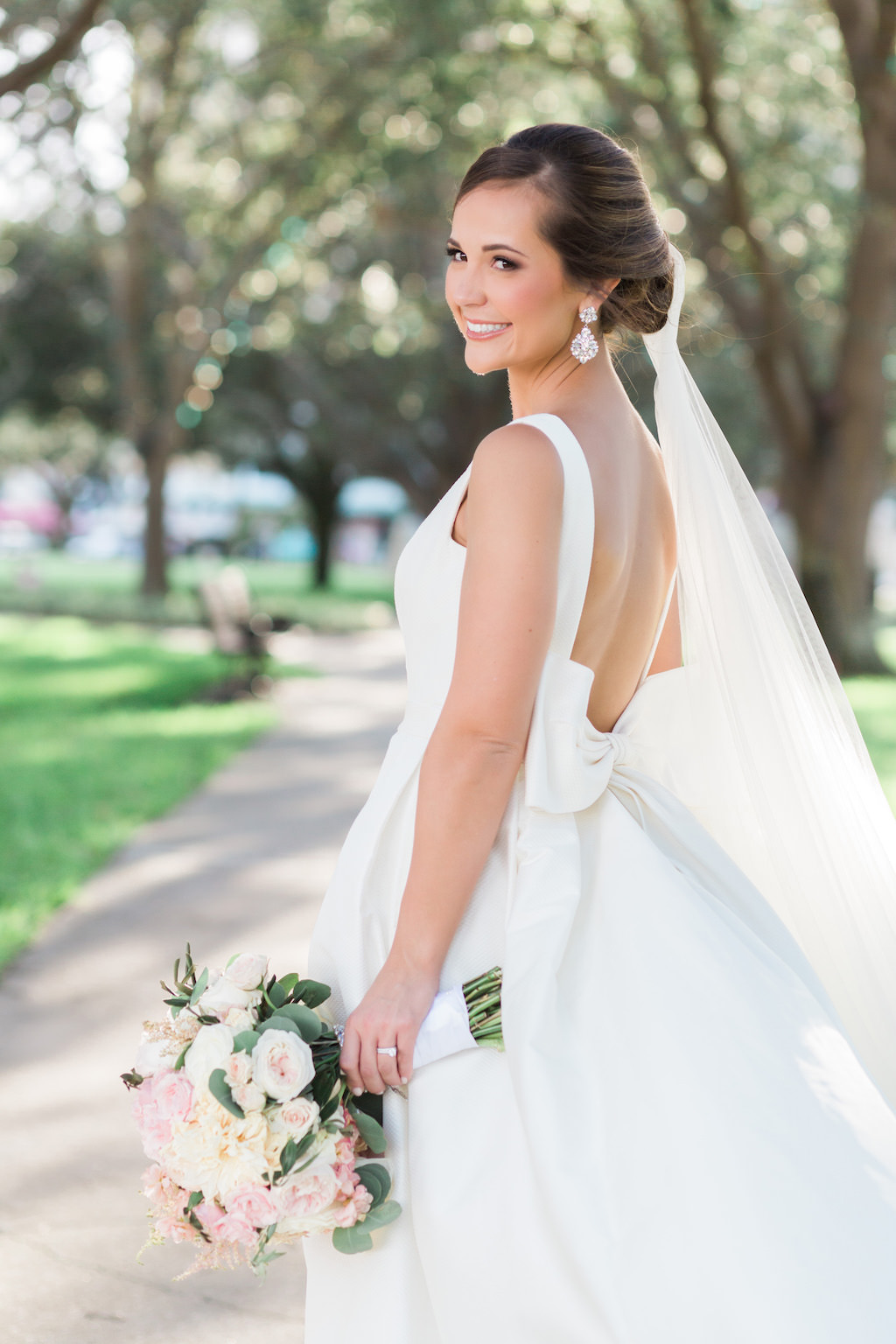 Outdoor Park Bridal Wedding Portrait in Open Back with Bow Rosa Clara Bridal Dress, with Blush Pink and White Peony Bouquet with Greenery, Comb Veil and Large Drop Earrings | St Pete Wedding Hair and Makeup Michele Renee The Studio