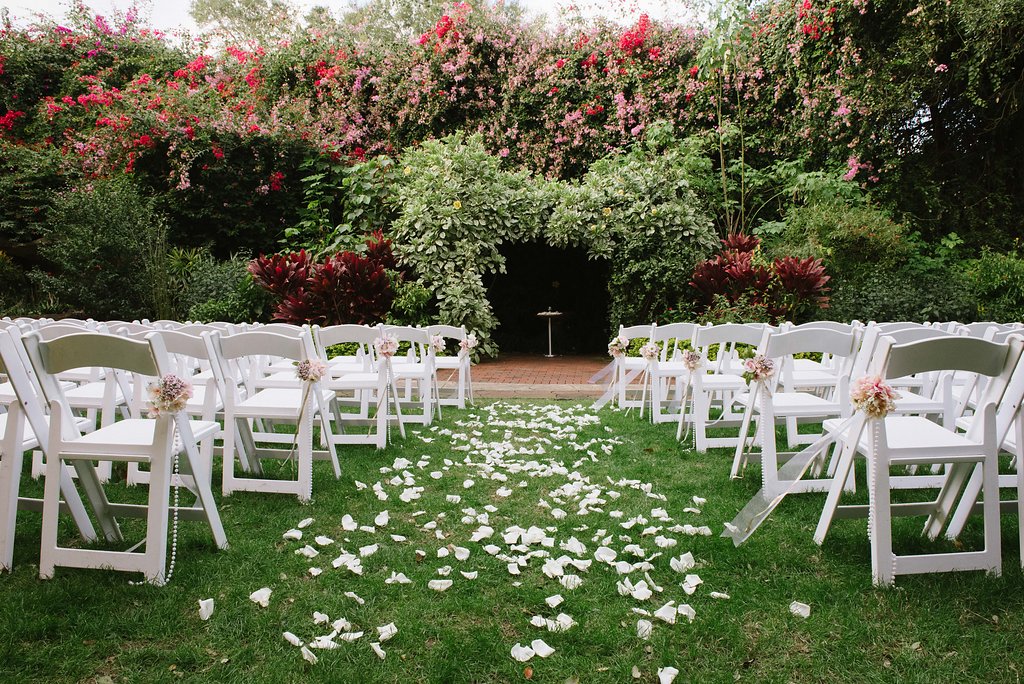 Outdoor Garden Wedding Ceremony Decor with White Folding Chairs with Pink and White Flowers, Pearl Beads, and Gold Ribbon | St. Pete Wedding Ceremony Venue The Sunken Gardens