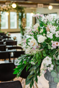 Indoor Industrial Wedding Ceremony Decor with Floral and Greenery Arch, White and BLush Flower with Natural Greenery in Tall Planter, and Mismatched Dark Wooden Chairs