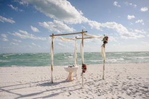Outdoor Beach Wedding Ceremony Decor with Bamboo Ceremony Arch With Wrapped White Draping and Red and Pink with Greenery Tropical Flowers | Longboat Key Beach Wedding Planner NK Productions