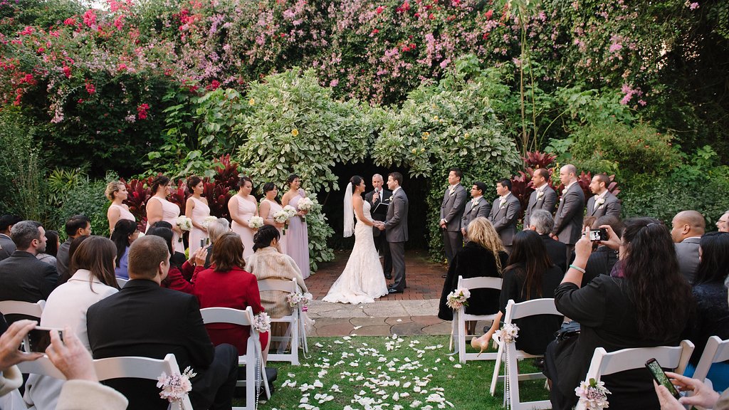 Outdoor Garden Wedding Ceremony Portrait, with White Folding Chairs with Pink and White Flowers, Pearl Beads, and Gold Ribbon, Bridesmaids in Off the Shoulder Blush PInk Dresses, Groomsmen in Gray Suits | St Pete Wedding Ceremony Venue The Sunken Gardens