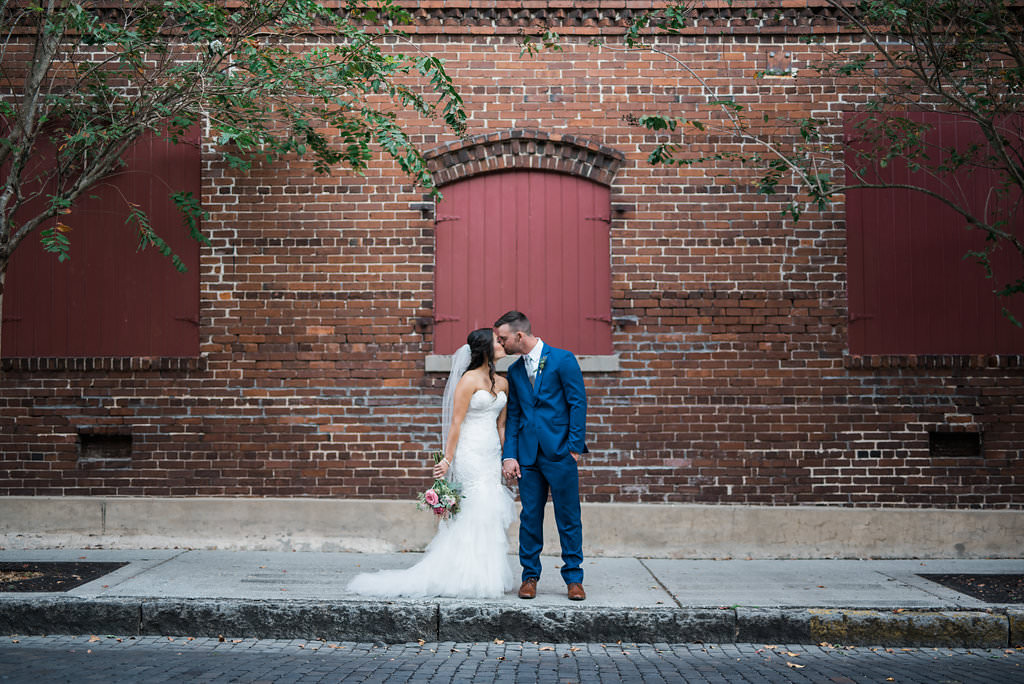 Downtown Tampa/Ybor City Industrial Chic Wedding Portrait, Bride in Mermaid Enzoani Dress with Pink Bouquet with Greenery, Groom in Blue Suit with Brown Shoes | Tampa Wedding Photographer Kera Photography