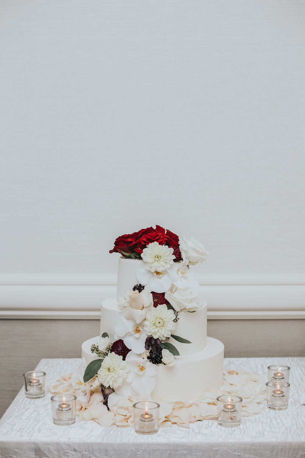 Three Tier Round White Wedding Cake with White, Red, and Greenery Florals with Flower Petals and Votive Candles | Clearwater Beach Wedding Cake Bakery A Piece of Cake