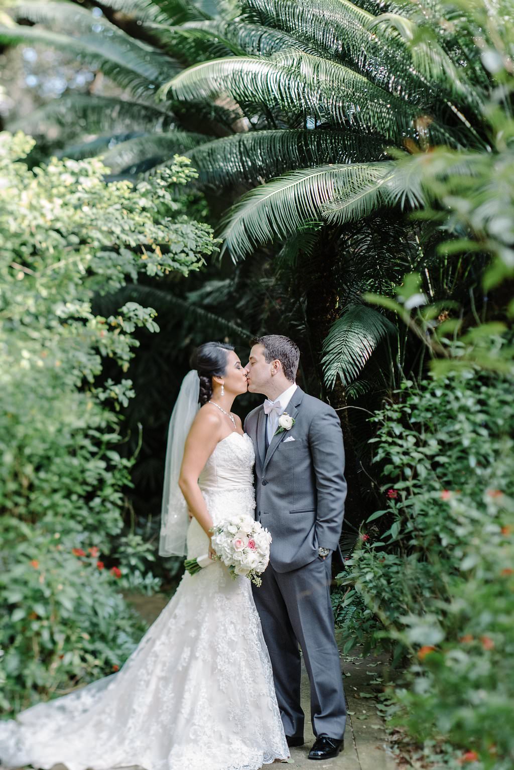 Outdoor Tropical Garden Bride and Groom Wedding Portrait, Bride in Strapless Lace Allure Bridal Dress with Comb Veil, Groom in Grey Suit | St Pete Wedding Venue Sunken Gardens