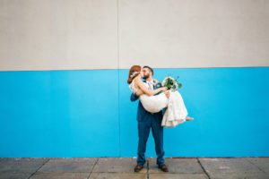 Downtown Tampa Creative Wedding Portrait, Bride in Sweetheart Lace Stella York Dress with White and Greenery Bouquet, Groom in Blue Suit