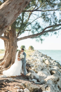 Outdoor Beach Wedding Bride and Groom Portrait, Groom in Gray Suit with Blush Pink Tie and Rose Boutonniere, Bride in Halter Ballgown Hayley Paige Wedding Dress with White Rose Bouquet and Jeweled Headband | Whimsical Clearwater Beach Wedding