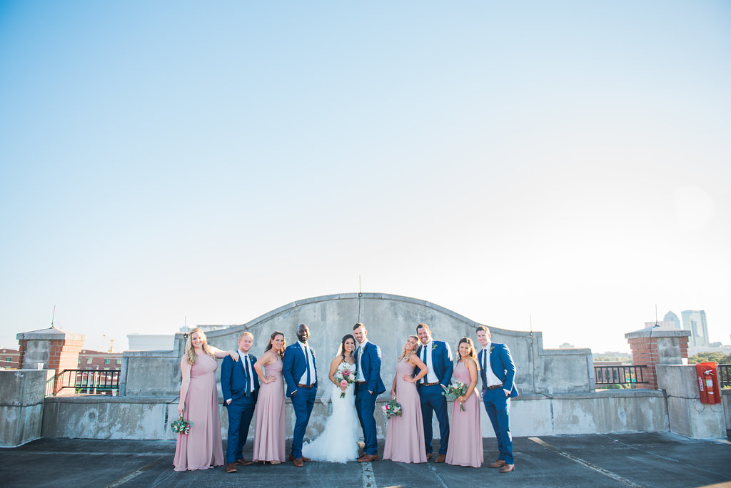 Downtown Tampa Skyline/Ybor City Industrial Chic Rooftop Wedding Party Portrait, Bride in Mermaid Enzoani Dress with Pink Bouquet with Greenery, Groom and Groomsmen in Blue Suit with Brown Shoes, Bridesmaids in Blush Azazie Dresses | Tampa Wedding Photographer Kera Photography