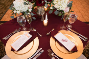 Gold and Burgundy FSU Alumni Wedding Reception Table Decor with small Red Rose, White Hydrangea, Blush Pink Floral and Greenery Centerpieces and Gold Printed Menu