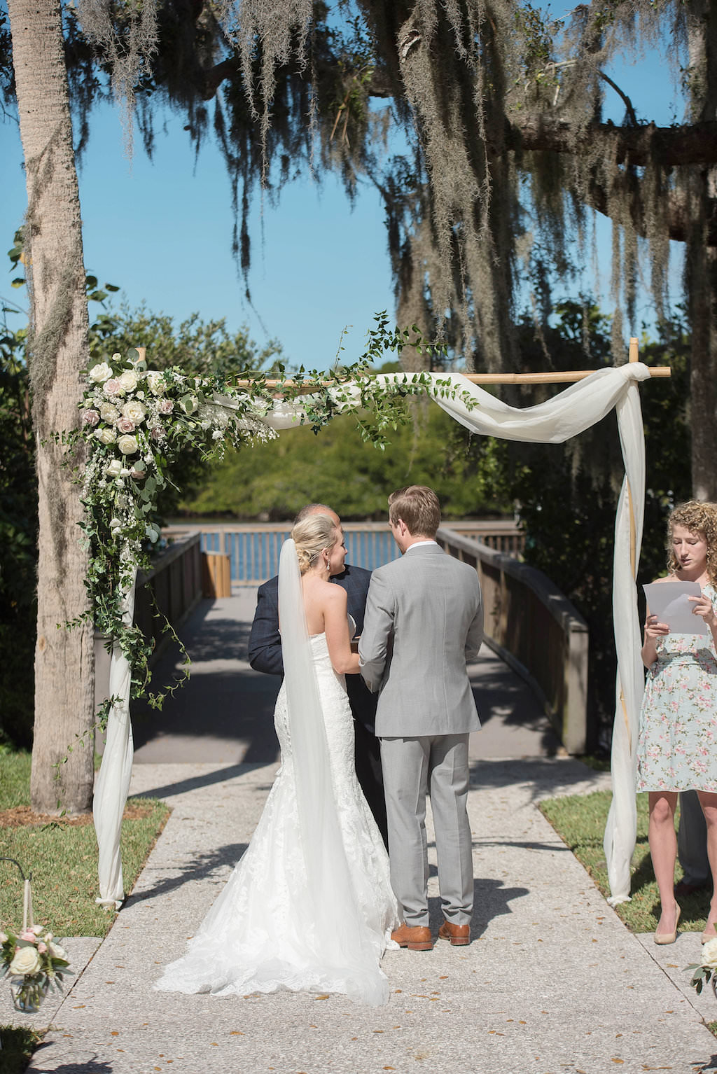 Outdoor Waterfront Garden Wedding Ceremony Portrait under white draped Ceremony Arch with White Rose and Natural Greenery Flowers | Sarasota Wedding Photographer Kristen Marie Photography | Historic Venue The Edson Keith Mansion